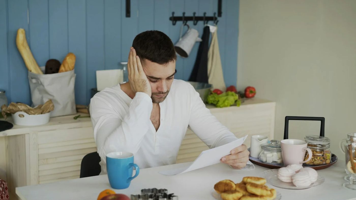 Mann stützt am Küchentisch besorgt den Kopf in die Hand und liest ein Schreiben